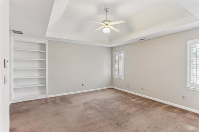 empty room featuring a raised ceiling, built in features, carpet, and visible vents