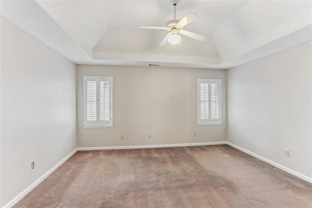 unfurnished room with plenty of natural light, ceiling fan, a raised ceiling, and carpet