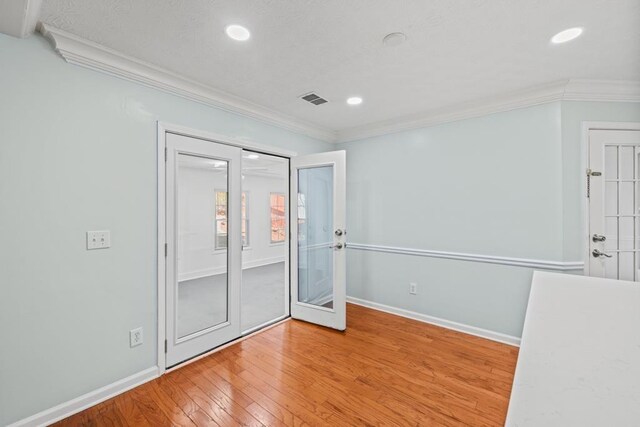 spare room featuring light wood-style floors, baseboards, visible vents, and crown molding