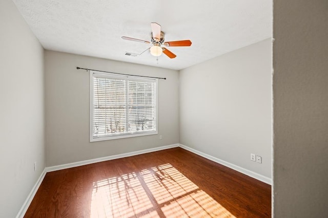 spare room featuring a ceiling fan, visible vents, baseboards, and wood finished floors