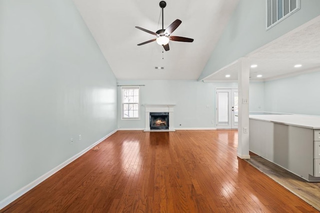 unfurnished living room featuring wood-type flooring, visible vents, high vaulted ceiling, a lit fireplace, and baseboards