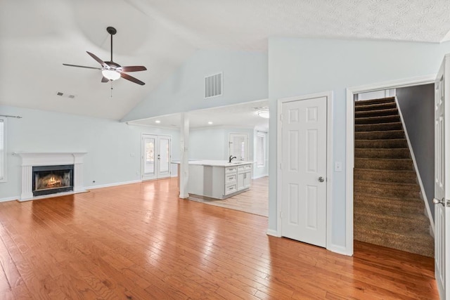 unfurnished living room with a warm lit fireplace, visible vents, a ceiling fan, stairway, and light wood-type flooring