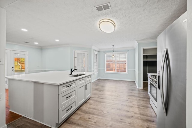 kitchen featuring a kitchen island with sink, stainless steel appliances, a sink, visible vents, and light wood-type flooring