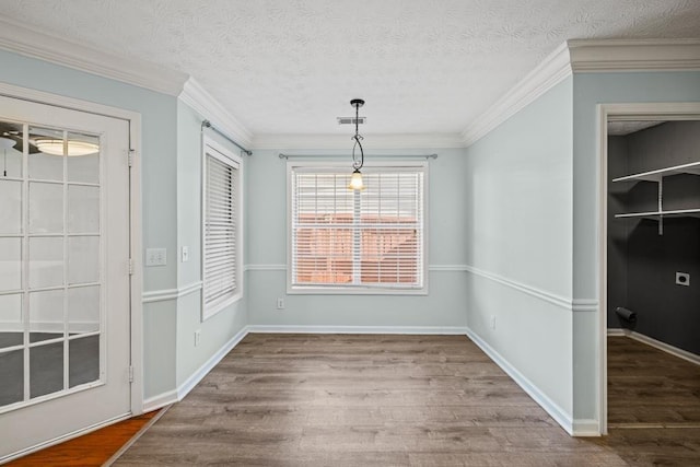 unfurnished dining area featuring ornamental molding, a textured ceiling, baseboards, and wood finished floors