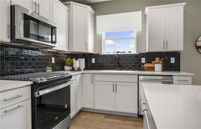 kitchen with decorative backsplash, sink, light wood-type flooring, stainless steel appliances, and white cabinets