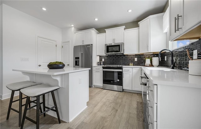 kitchen with appliances with stainless steel finishes, white cabinets, a breakfast bar, and sink