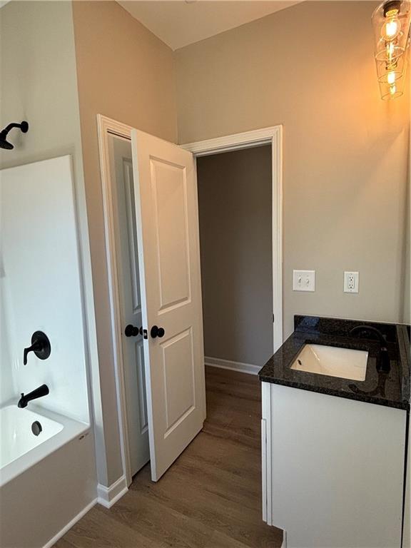 bathroom with bathtub / shower combination, baseboards, wood finished floors, and vanity