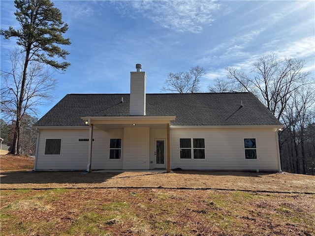 back of house featuring a shingled roof, a chimney, and a yard