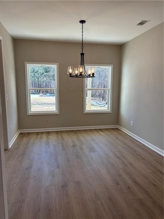 unfurnished dining area with visible vents, a notable chandelier, baseboards, and wood finished floors