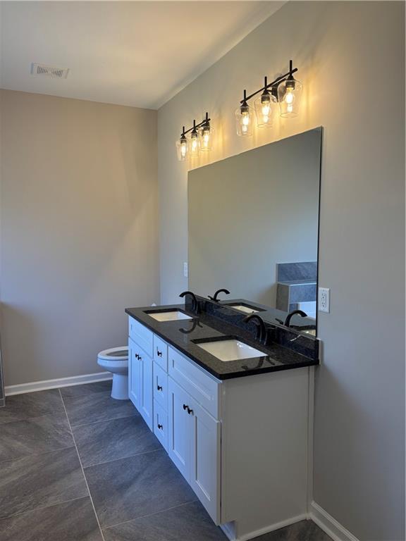 bathroom with double vanity, baseboards, toilet, and a sink