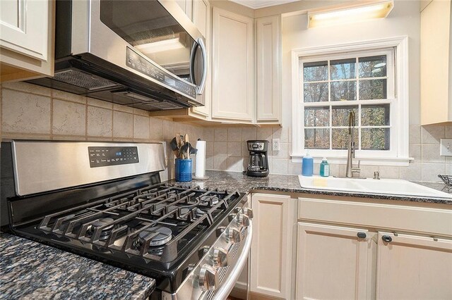 kitchen with decorative backsplash, appliances with stainless steel finishes, dark stone counters, and sink