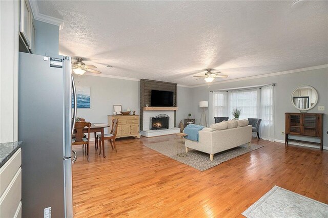 living room with crown molding, ceiling fan, light hardwood / wood-style floors, and a textured ceiling