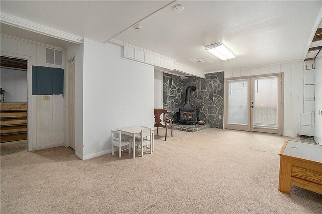 basement featuring carpet flooring, a wood stove, crown molding, and french doors