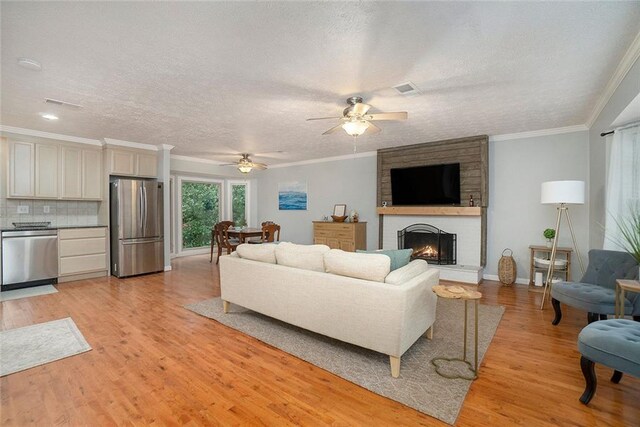 living room with ceiling fan, a brick fireplace, light hardwood / wood-style flooring, crown molding, and a textured ceiling