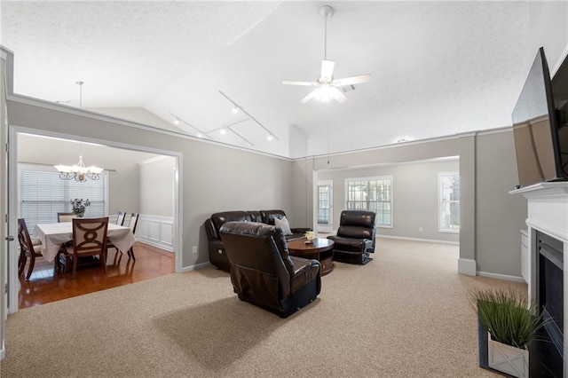 carpeted living room featuring a fireplace with flush hearth, lofted ceiling, ceiling fan with notable chandelier, a textured ceiling, and baseboards