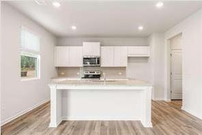 kitchen with white cabinets, an island with sink, appliances with stainless steel finishes, light countertops, and light wood-style floors