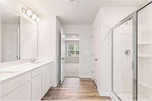 bathroom featuring double vanity, a stall shower, and wood finished floors