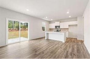 kitchen featuring white cabinets, stainless steel microwave, wood finished floors, a kitchen island with sink, and light countertops