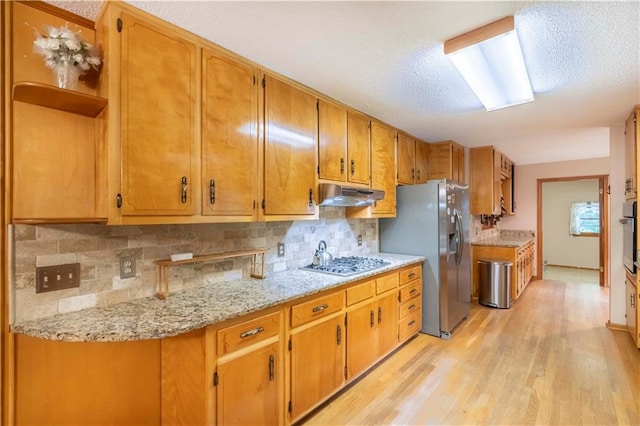 5670 Lanny Dr, Powder Springs, GA 30127 - kitchen featuring under cabinet range hood, appliances with stainless steel finishes, light wood-style floors, decorative backsplash, and a textured ceiling