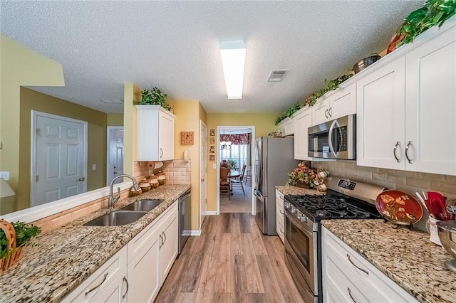 626 Dahoma Trl, Woodstock, GA 30188 - kitchen with appliances with stainless steel finishes, a sink, white cabinetry, light wood-style floors, and decorative backsplash