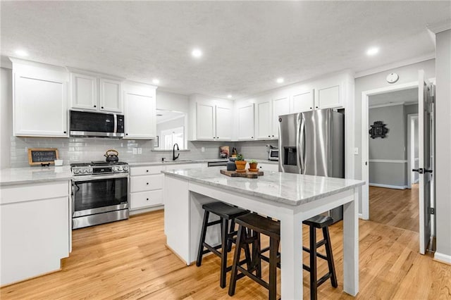 kitchen with light stone counters, a breakfast bar area, white cabinets, and appliances with stainless steel finishes