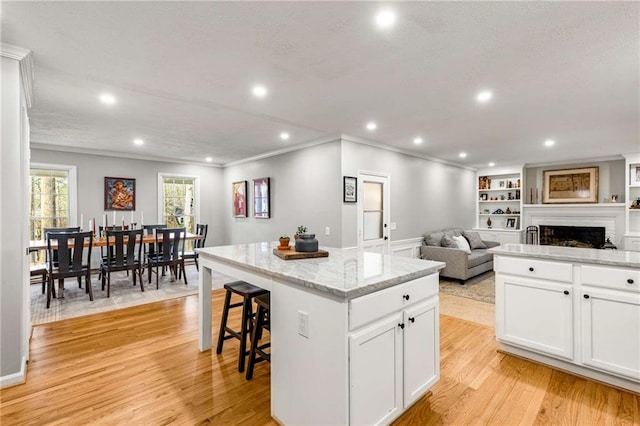 kitchen with light hardwood / wood-style flooring, light stone countertops, a kitchen island, and white cabinets