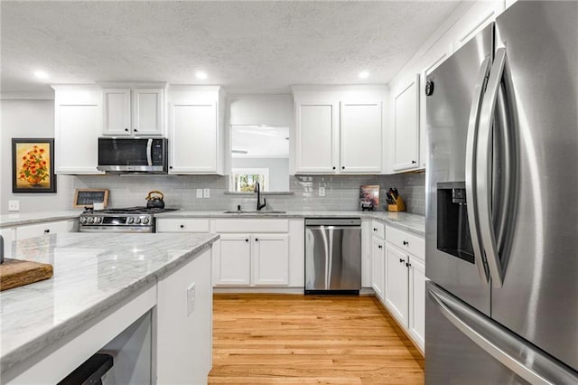 kitchen with sink, white cabinetry, light hardwood / wood-style flooring, stainless steel appliances, and light stone countertops