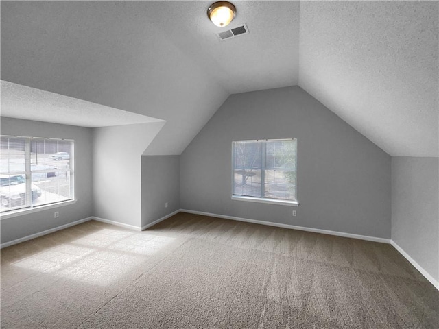 bonus room featuring lofted ceiling, a textured ceiling, and light colored carpet