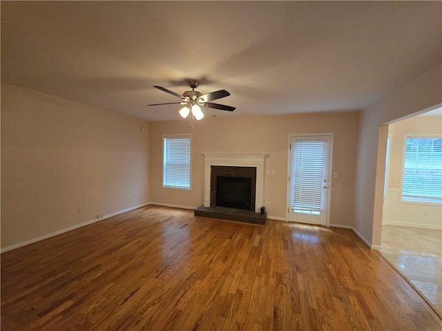 unfurnished living room featuring a brick fireplace, wood-type flooring, and ceiling fan