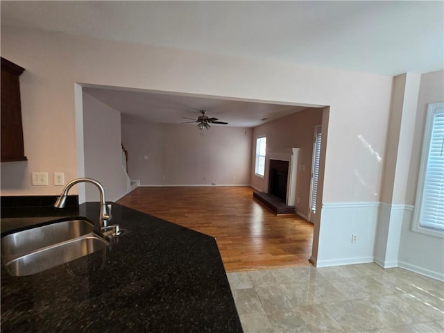 kitchen with sink, light hardwood / wood-style flooring, ceiling fan, dark stone countertops, and dark brown cabinetry