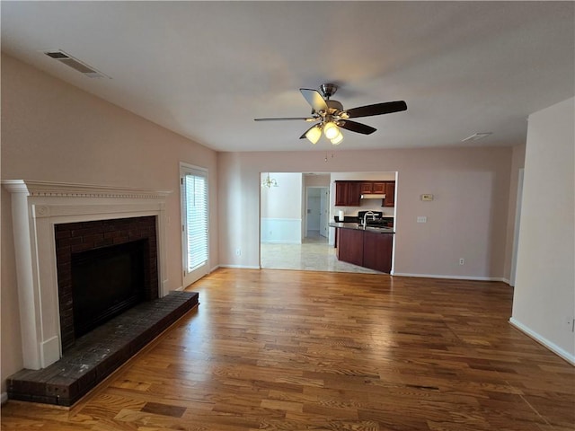 unfurnished living room with wood-type flooring, sink, ceiling fan, and a fireplace