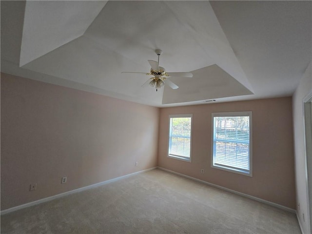 carpeted spare room with a raised ceiling and ceiling fan