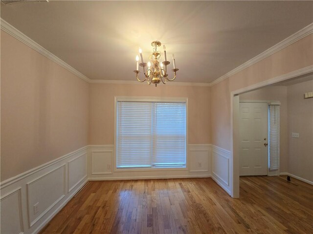 spare room with wood-type flooring, crown molding, and an inviting chandelier