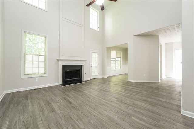 unfurnished living room with ceiling fan, a towering ceiling, dark hardwood / wood-style flooring, and a healthy amount of sunlight