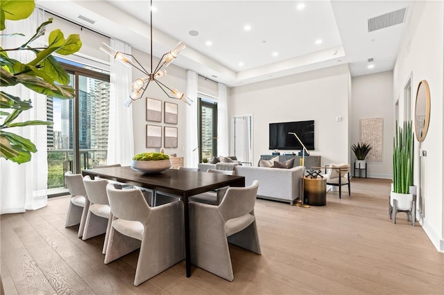 dining area featuring a notable chandelier, a raised ceiling, light hardwood / wood-style flooring, and a wealth of natural light