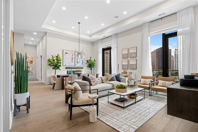 living room featuring a raised ceiling, a chandelier, and light wood-type flooring