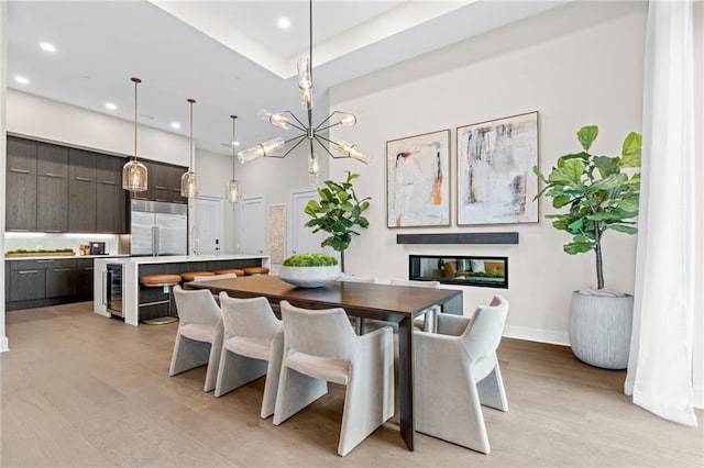 dining space with sink, beverage cooler, a chandelier, and light hardwood / wood-style floors