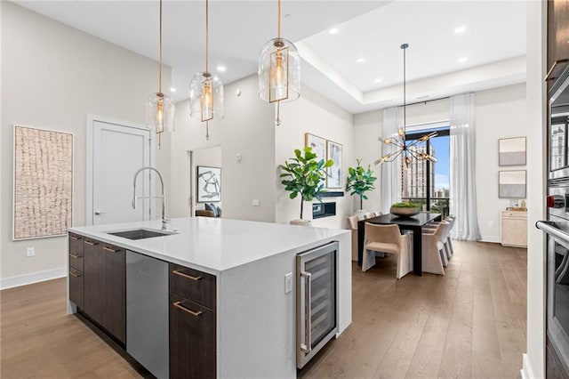 kitchen with dark brown cabinetry, sink, a center island with sink, dishwasher, and beverage cooler