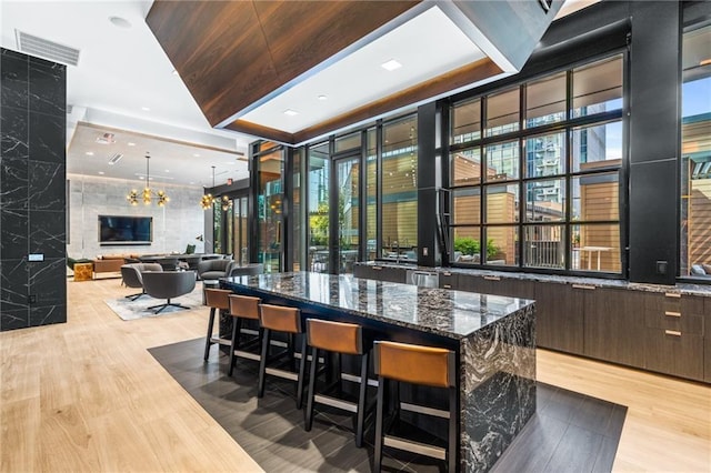 bar featuring dark stone countertops, tile walls, a chandelier, dark brown cabinets, and light wood-type flooring