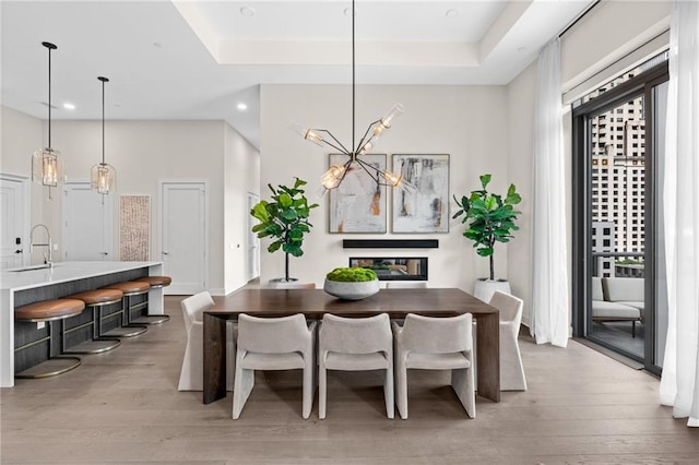 dining area with sink, a tray ceiling, light hardwood / wood-style floors, and a chandelier