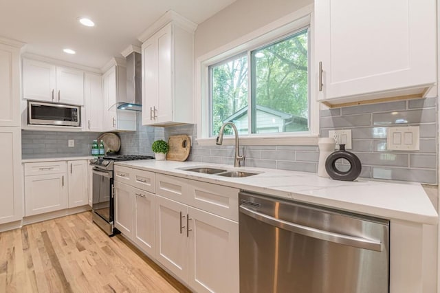 kitchen with stainless steel appliances, wall chimney exhaust hood, a sink, and white cabinets