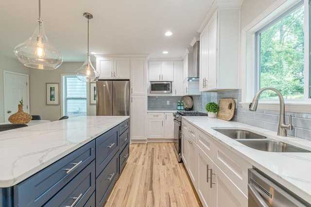 kitchen featuring light wood finished floors, backsplash, appliances with stainless steel finishes, white cabinets, and a sink