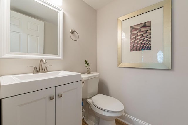 half bathroom featuring toilet, baseboards, and vanity