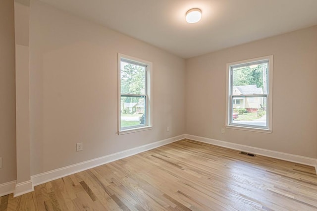 unfurnished room with a wealth of natural light, visible vents, light wood-style flooring, and baseboards