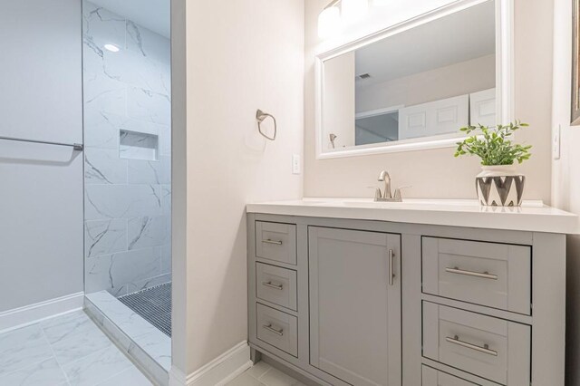 full bathroom with marble finish floor, a tile shower, vanity, and baseboards