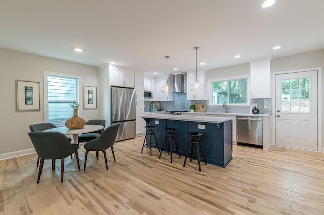 kitchen with a breakfast bar area, light countertops, appliances with stainless steel finishes, a kitchen island, and wall chimney range hood