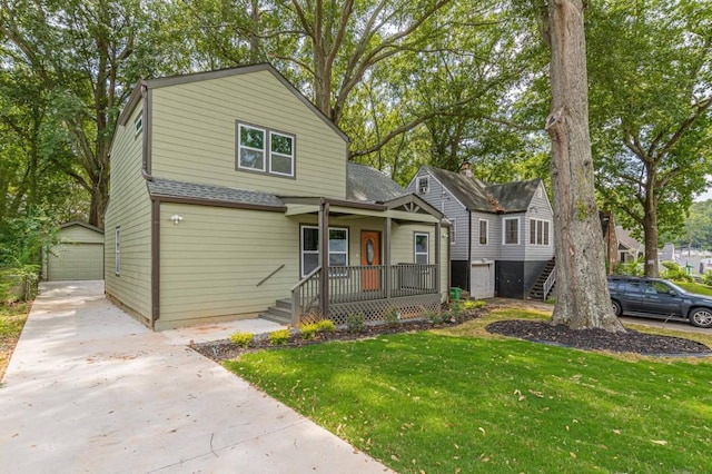 view of front of house featuring a shingled roof, a detached garage, an outbuilding, a porch, and a front yard