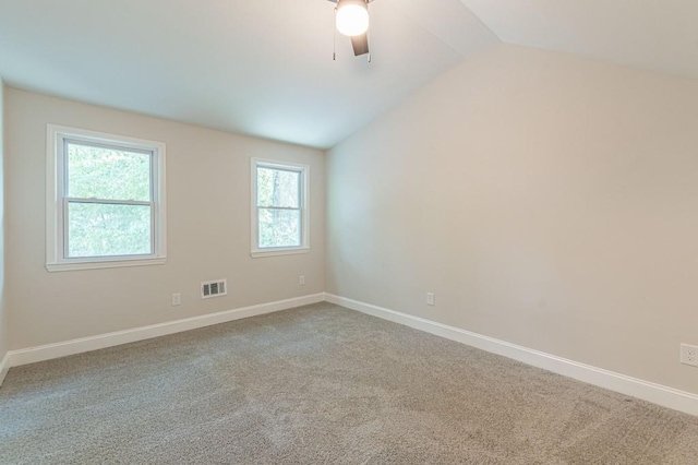 carpeted spare room featuring visible vents, vaulted ceiling, baseboards, and ceiling fan