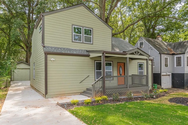 view of front of house with a detached garage, roof with shingles, an outdoor structure, a porch, and a front yard