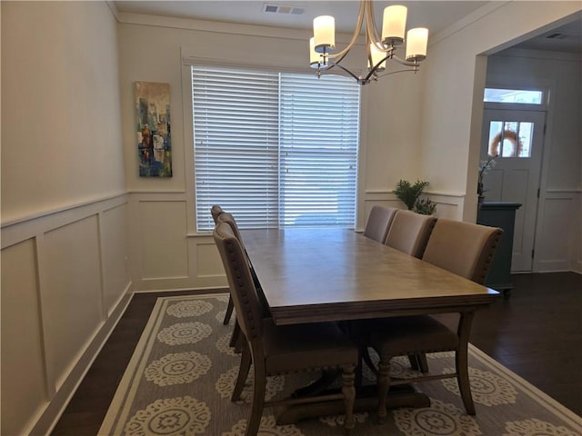 dining room with visible vents, dark wood-style flooring, crown molding, a decorative wall, and a chandelier